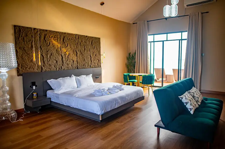 Spacious and elegant interior of the Deluxe Suite at Turtle Seaweed Resort featuring a large bed, teal sofa, and glass balcony doors.